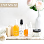 Collection of skincare products including bottles and a jar on a marble surface with flowers in the background.