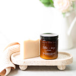 Pretty Farm Girl's fragrance free soap bar, and 5.4 glass amber jar of fragrance free Tallow + Honey Cream on a stone tray with soap and flowers in the background