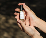 Hand holding a small bottle of Natural perfume oil-Cocoon with a blurred natural background