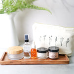 Set of skincare products on a wooden tray with a white pouch in the background