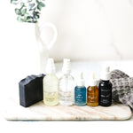 Set of skincare products on a marble surface with a white pitcher and plant in the background.