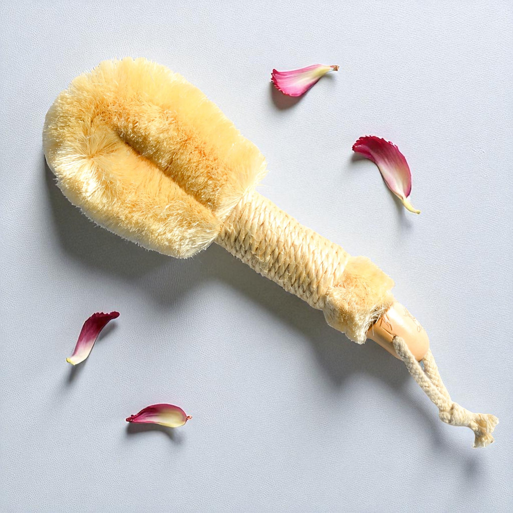 Body brush with natural bristles on a light gray background with flower petals.