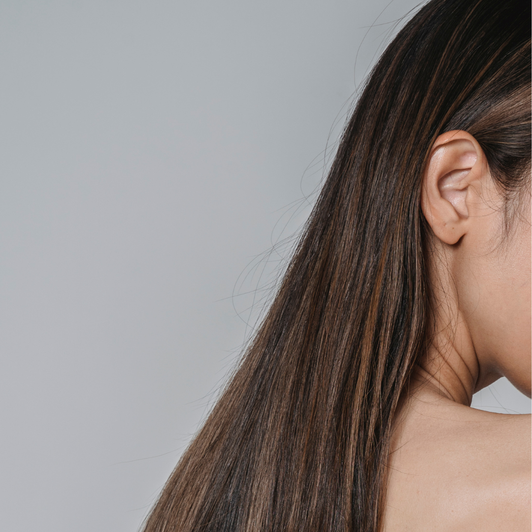 Close-up of a person's ear and straight brown hair against a plain background