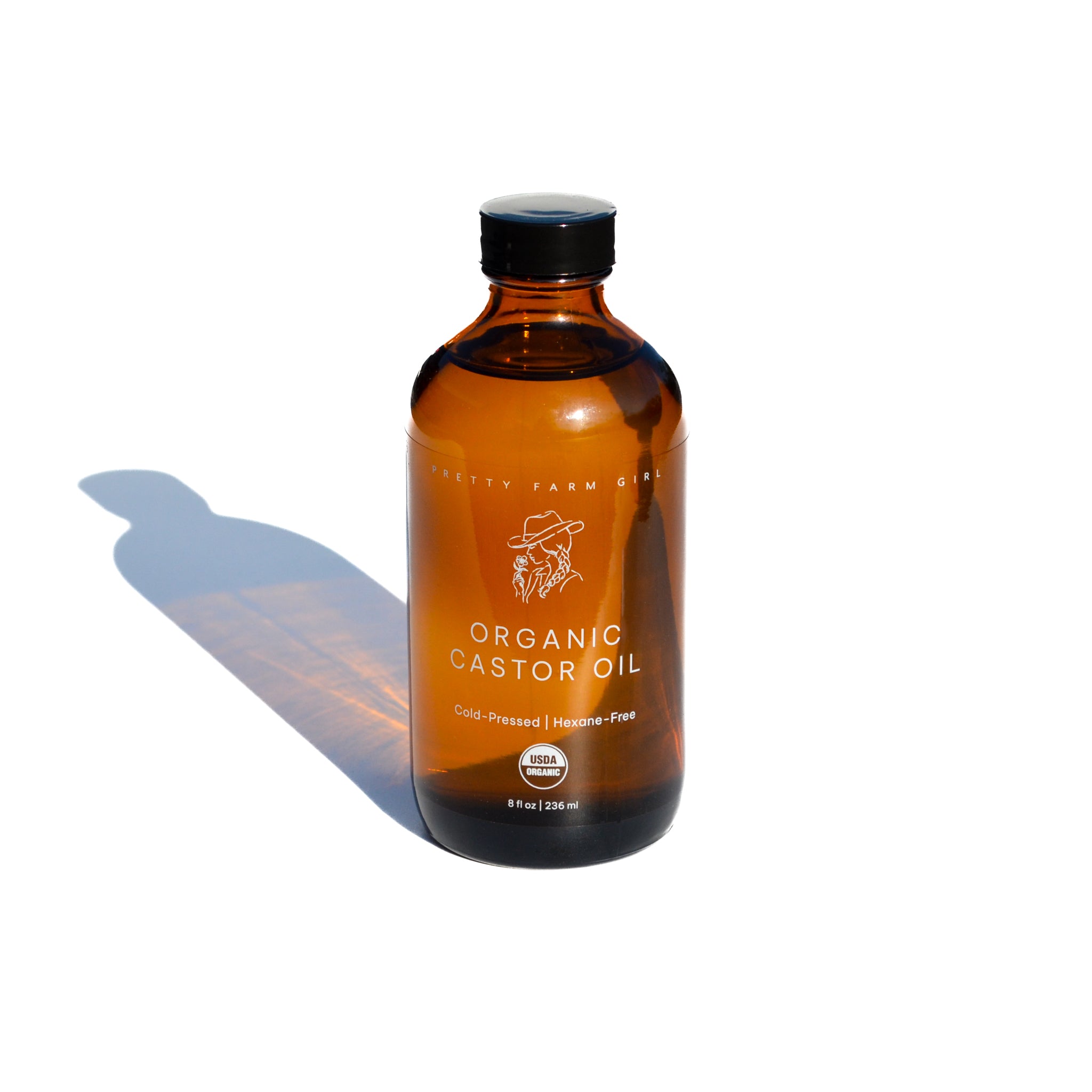 Amber bottle of a 8oz organic castor oil with light showing the color of the oil on a white background