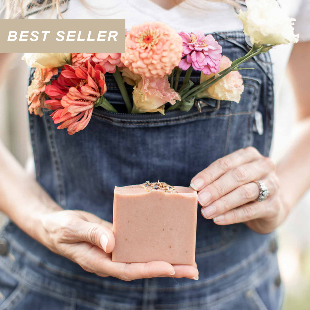 Wild Rose + Honey Handmade Tallow and Goat Milk Soap Bar held with fresh flowers in the background