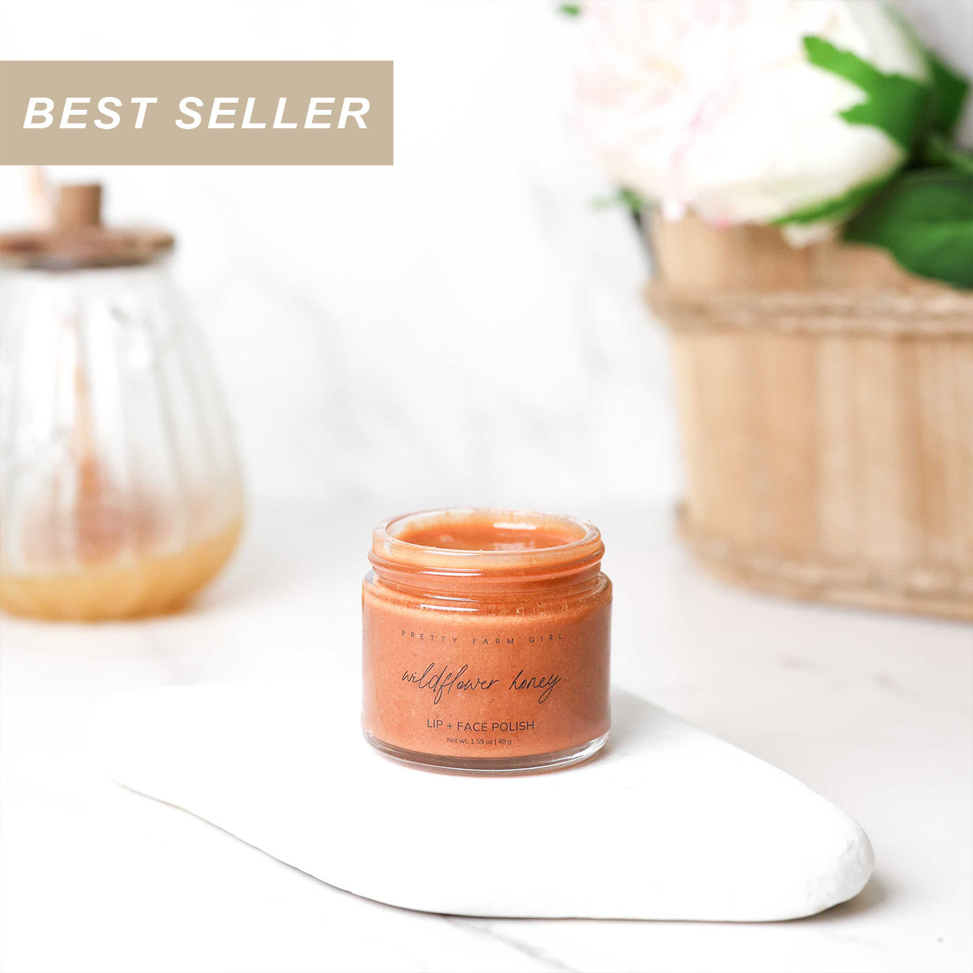 Jar of wildflower honey lip polish labeled 'Best Seller' on a white surface with a blurred background