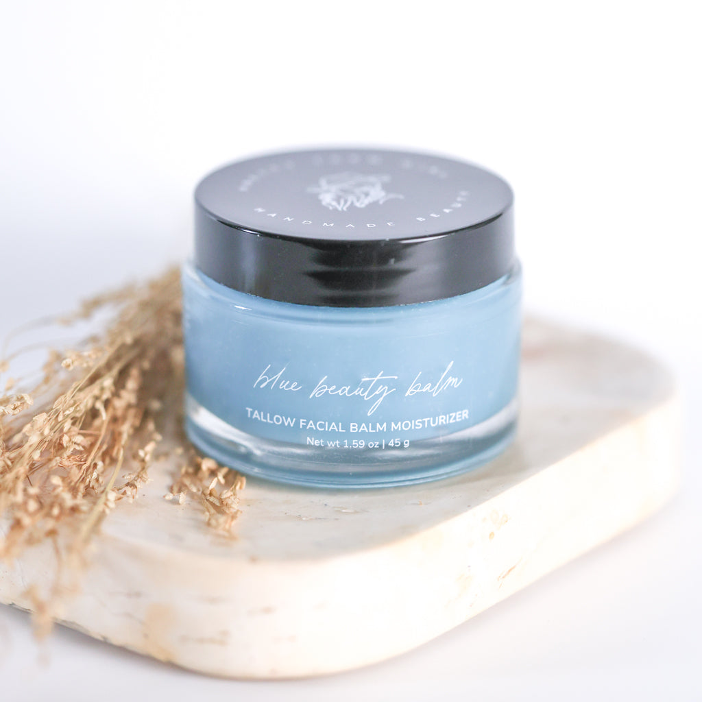 Pretty Farm Girl Blue Beauty Balm Soothing Tallow Face Balm jar on a white stone surface with dried botanical accents.
