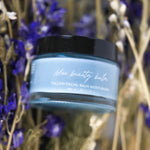 Blue beauty balm jar with black lid against a natural background of purple flowers and brown branches