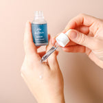 Serum bottle with dropper held by hands against a beige background