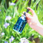 Hand holding a blue bottle labeled 'Blue Moon' against a green natural background