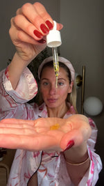 Woman holding a dropper with Brightening Serum dripping into her palm, wearing a floral robe.