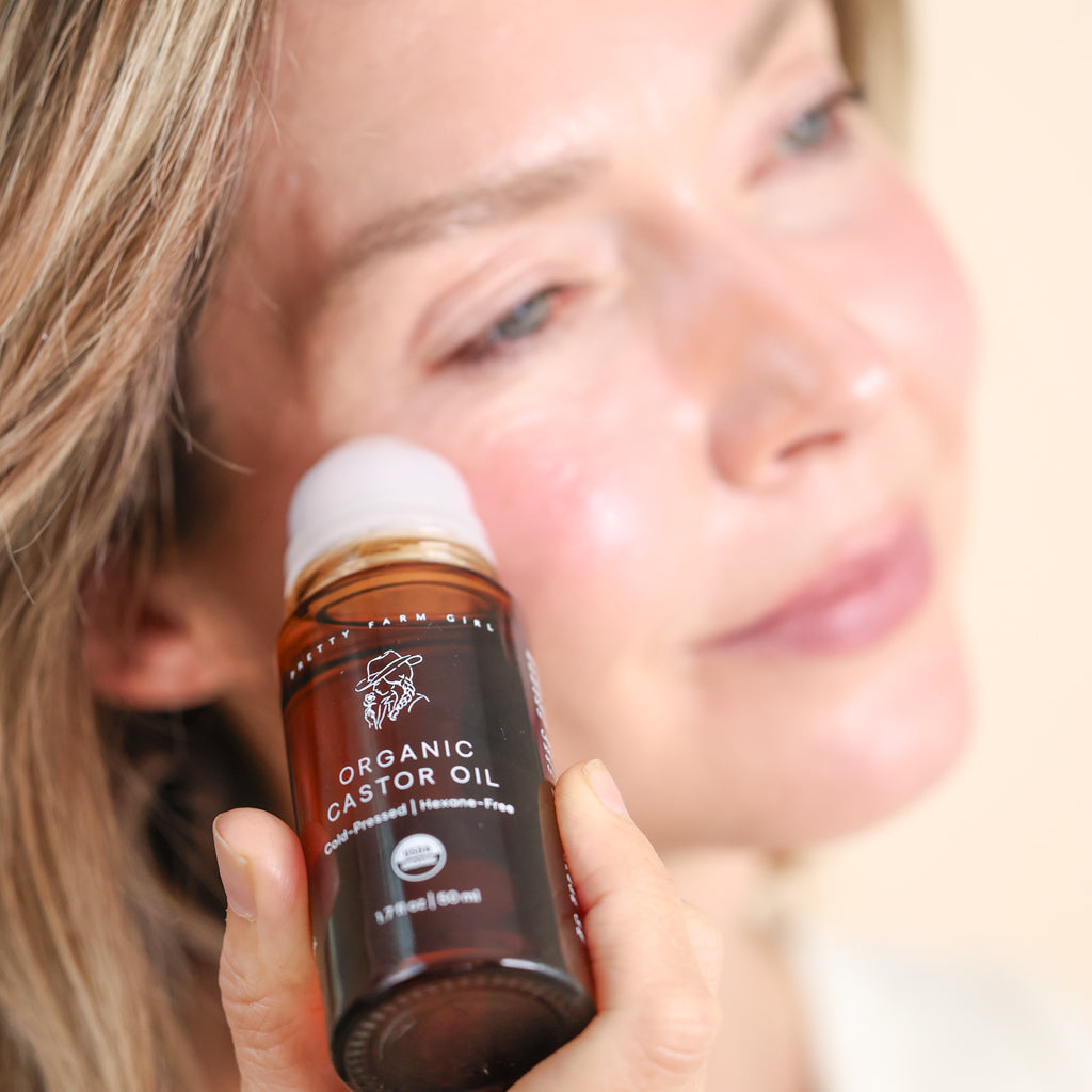 Woman applying Pretty Farm Girl Organic Castor Oil roller on face for brows and skin care