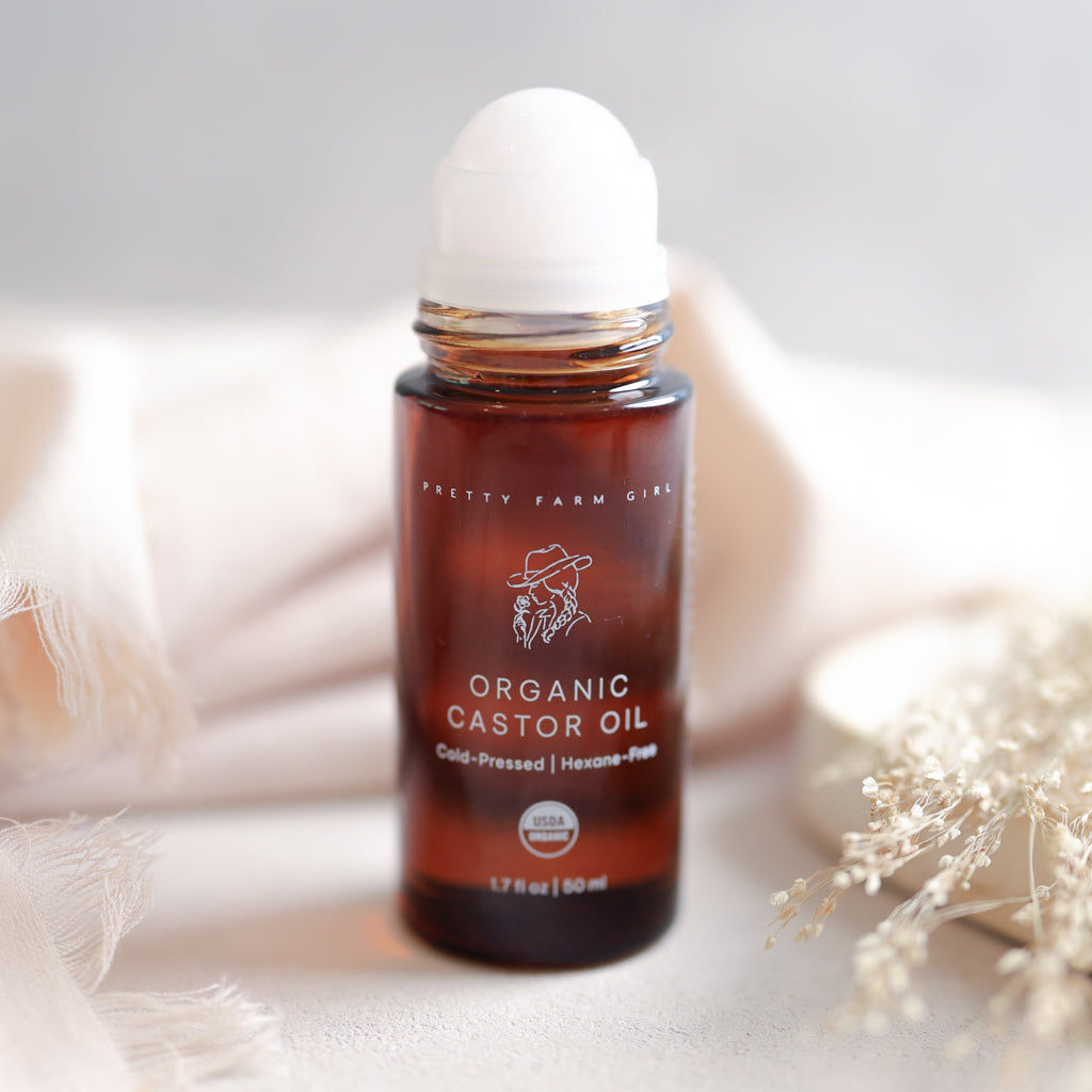 Pretty Farm Girl Organic Castor Oil roller bottle 1.7 fl oz with cap on neutral background with dried flowers