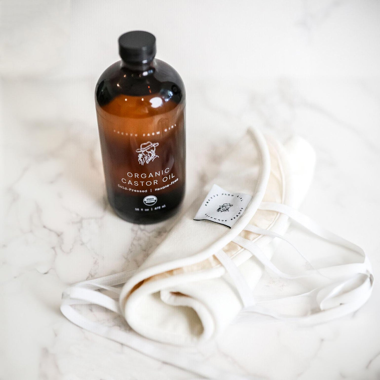 Bottle of organic castor oil and organic cotton castor oil pack on a white surface.