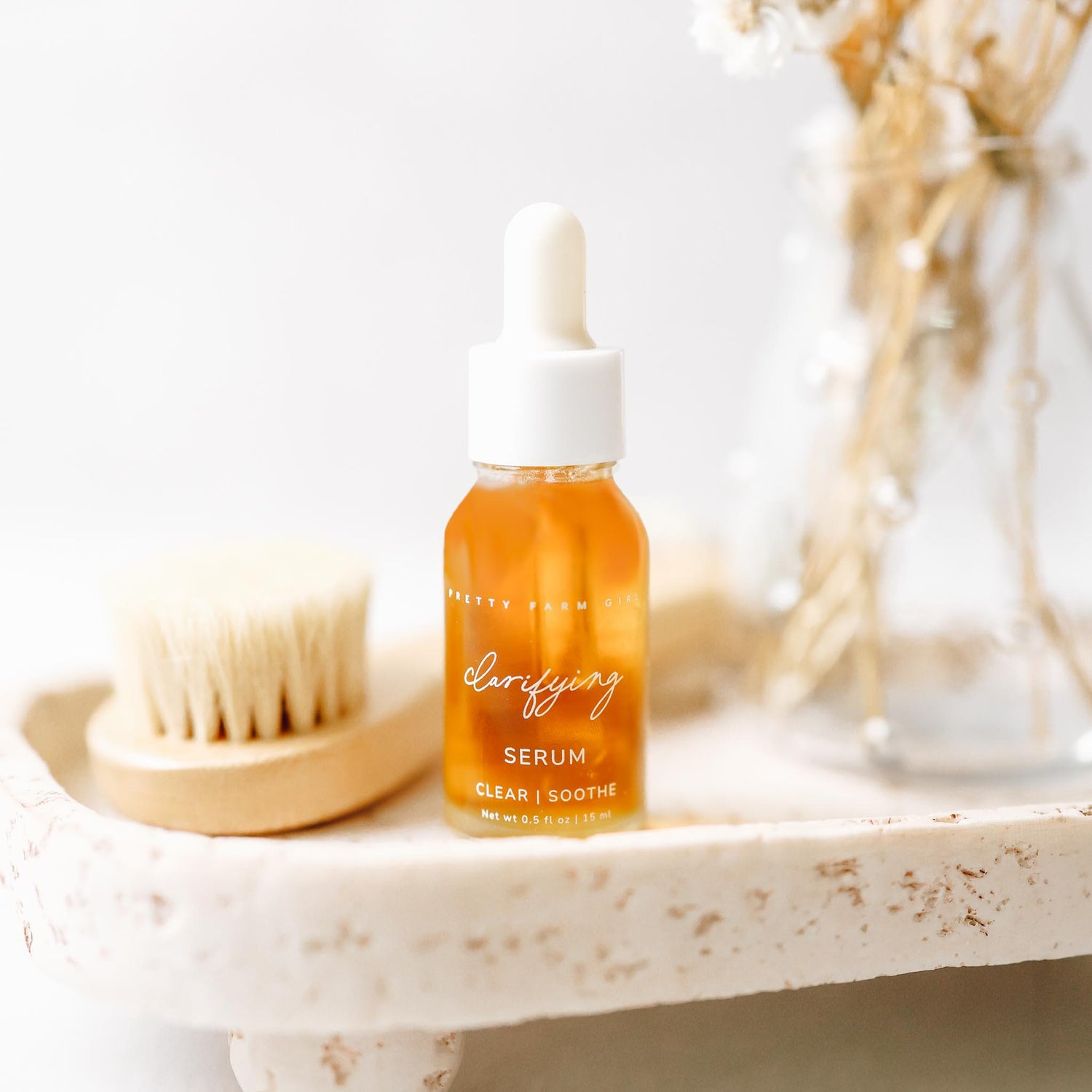 Serum bottle on a marble surface with a brush and jar in the background