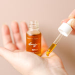 Hand holding a dropper with serum over a bottle labeled 'purifying serum' on a beige background