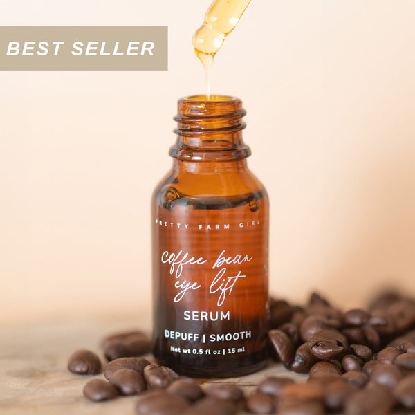0.5 oz glass brown serum bottle of Pretty Farm Girl's coffee bean eye lift serum with coffee beans on a wooden surface.