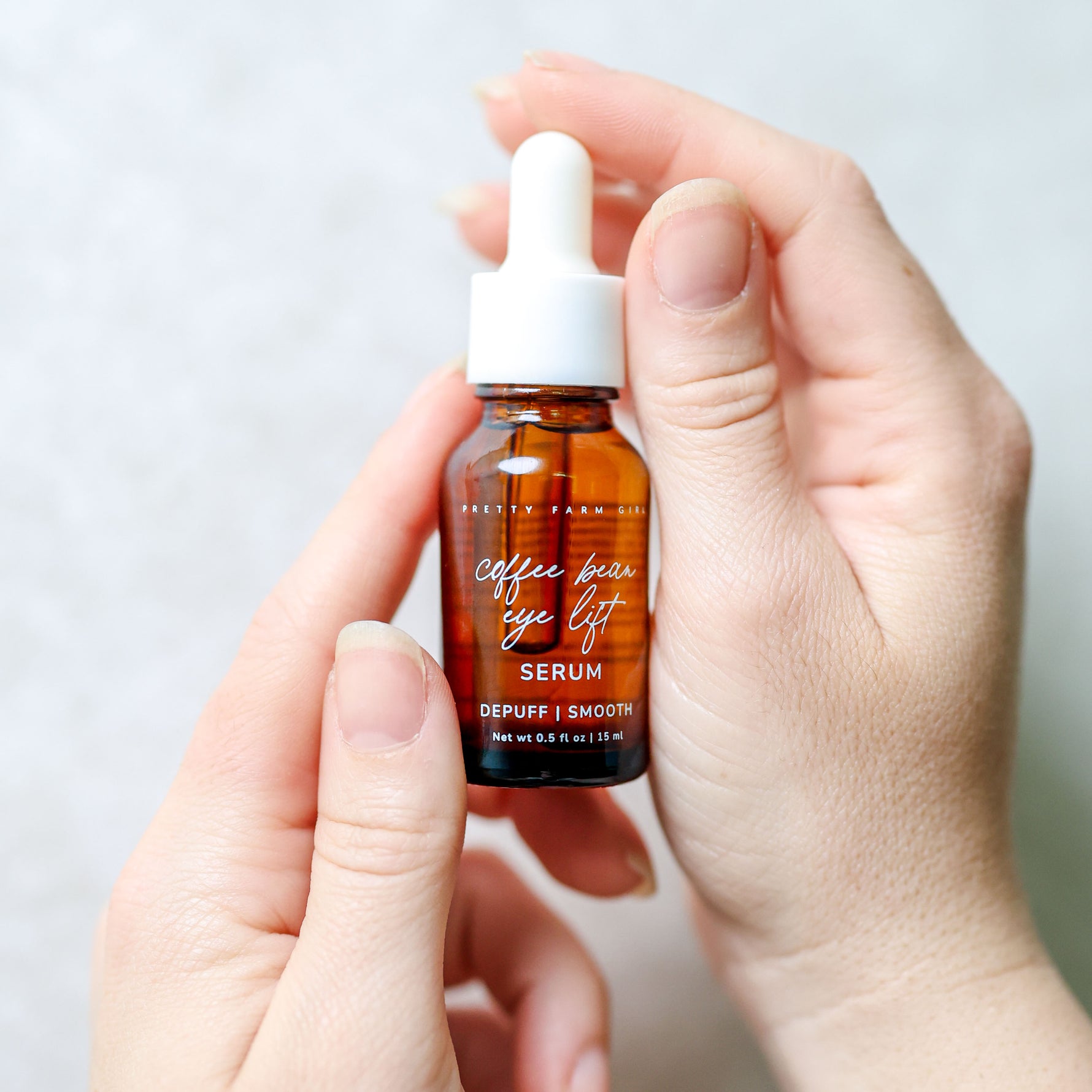 Coffee Bean Eye Lift Serum bottle held in hand on a bright white background
