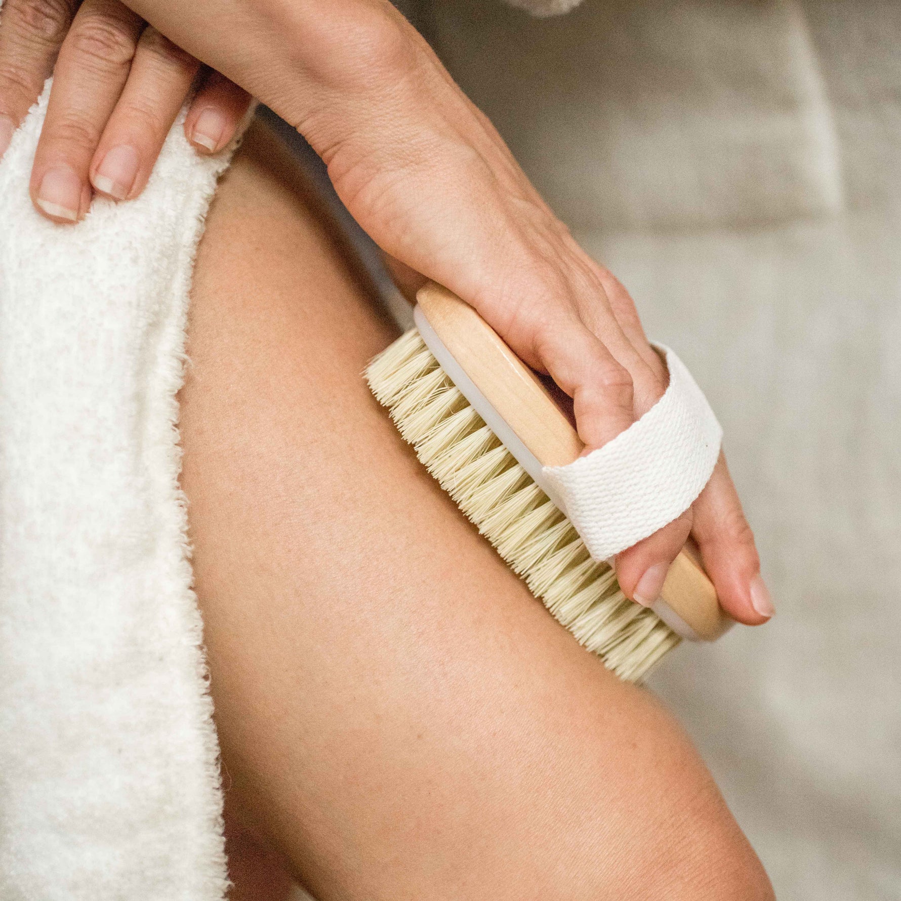 Person using a dry brush on their leg with a neutral background