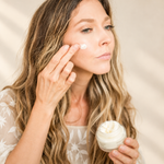Woman applying Pretty Farm Girl Fresh Face Cream to her cheek with her fingertips while holding the open jar.