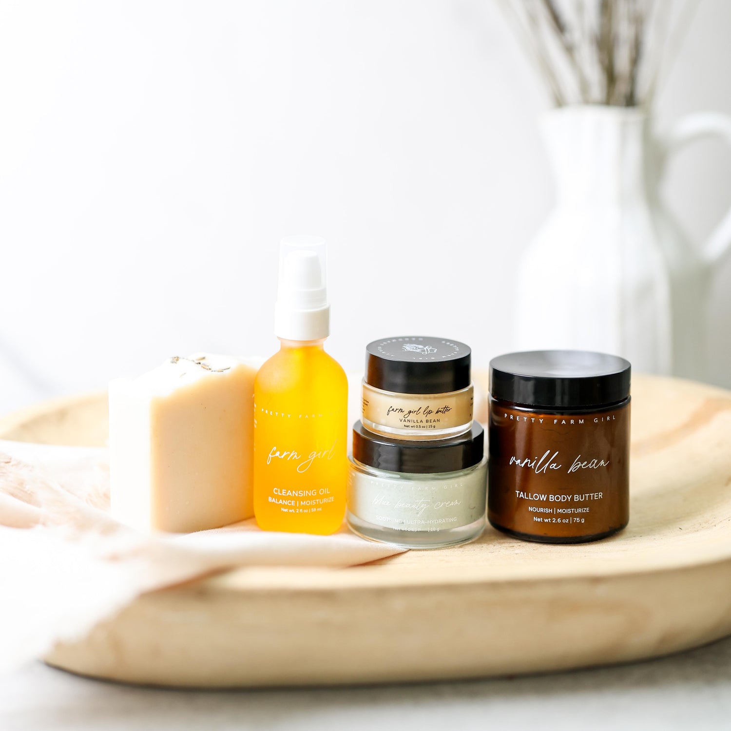 Collection of Pretty Farm Girl products including Wild Lavender tallow and goat milk soap, 2oz Farm girl cleansing oil, 0.5oz arm Girl vanilla bean beef tallow lip butter jar, 0.63oz Blue Beauty Beef Tallow Face Cream, 2.4oz Vanilla Bean tallow body butter, on a neutral background 