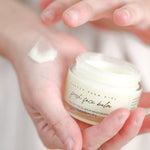 Pretty Farm Girl Fresh Face Cream jar held above a hand with cream texture.