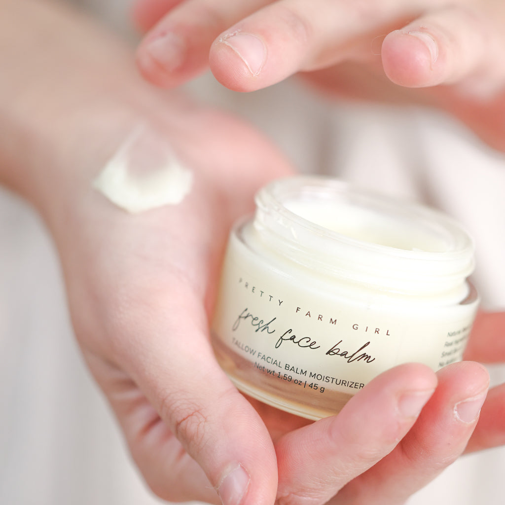 Pretty Farm Girl Fresh Face Cream jar held above a hand with cream texture.