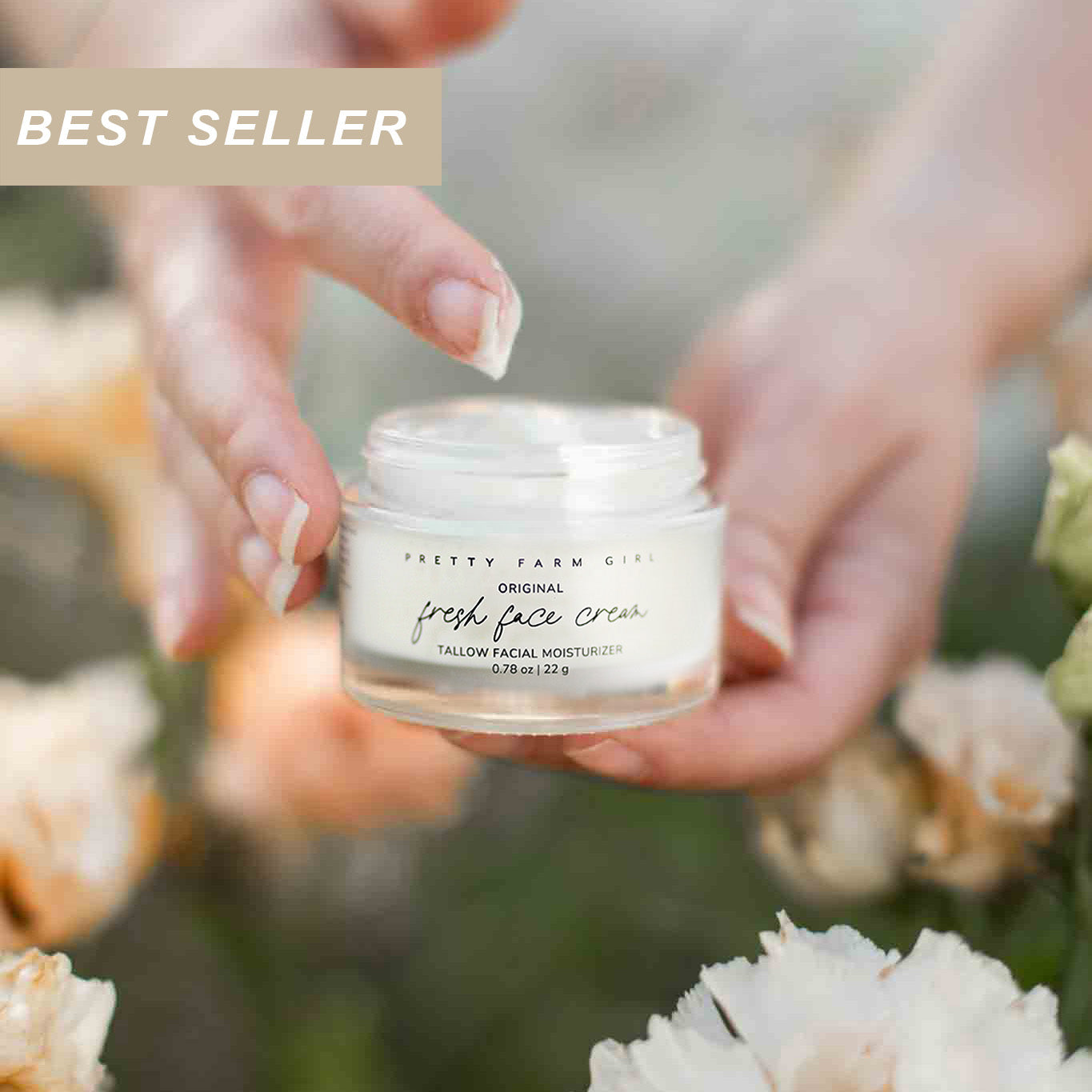 Person holding a 0.78oz glass jar of Pretty Farm Girl's beef tallow Original Fresh Face Cream with flowers in the background.