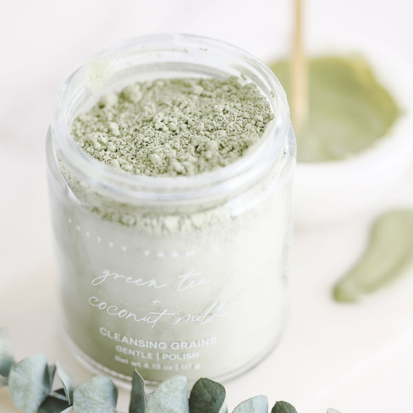 Green Tea and Coconut Milk Facial Cleansing Grains in glass jar with soft botanical background