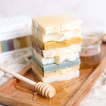 Stack of 8 layered sample sized soap bars with a honey dipper on a wooden tray