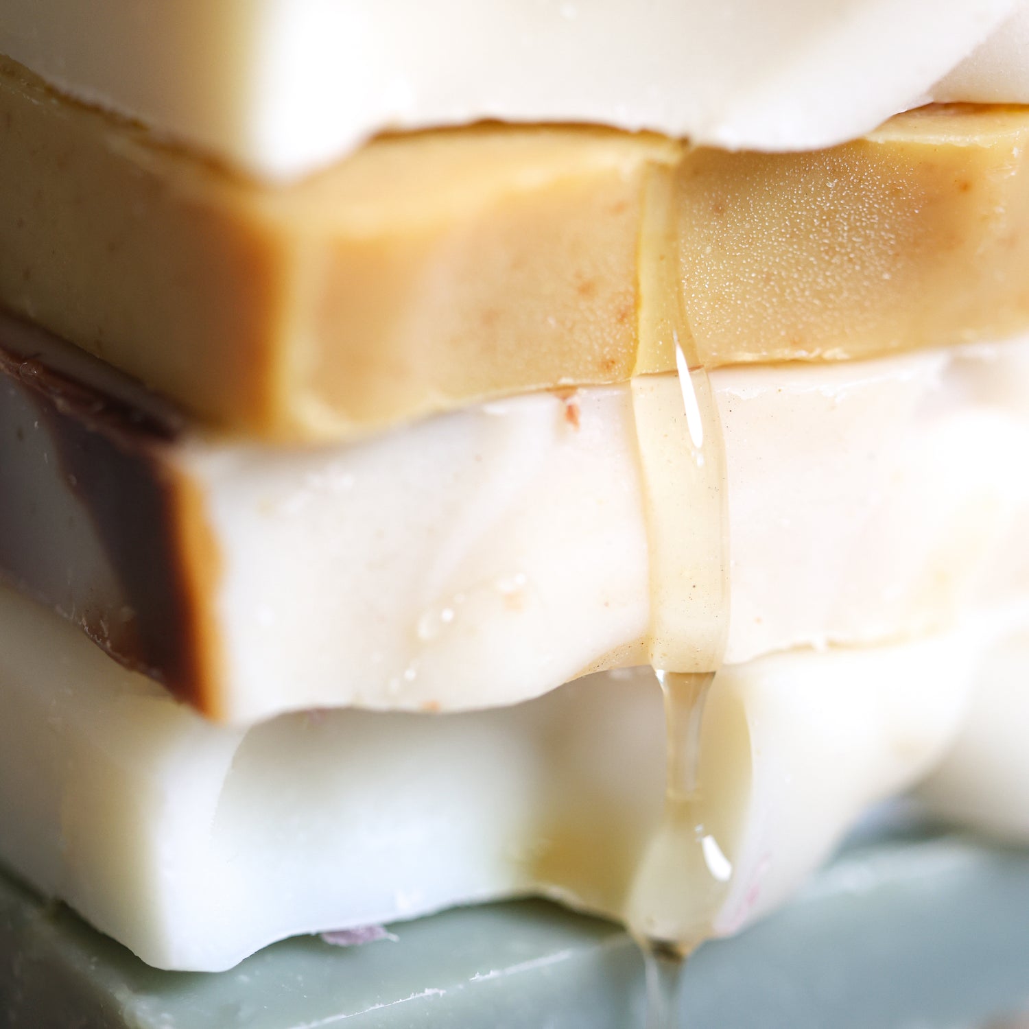 Close-up of layered sample sized soap bars with a focus on soap texture and color gradient. Honey is dripping down the soap stack.
