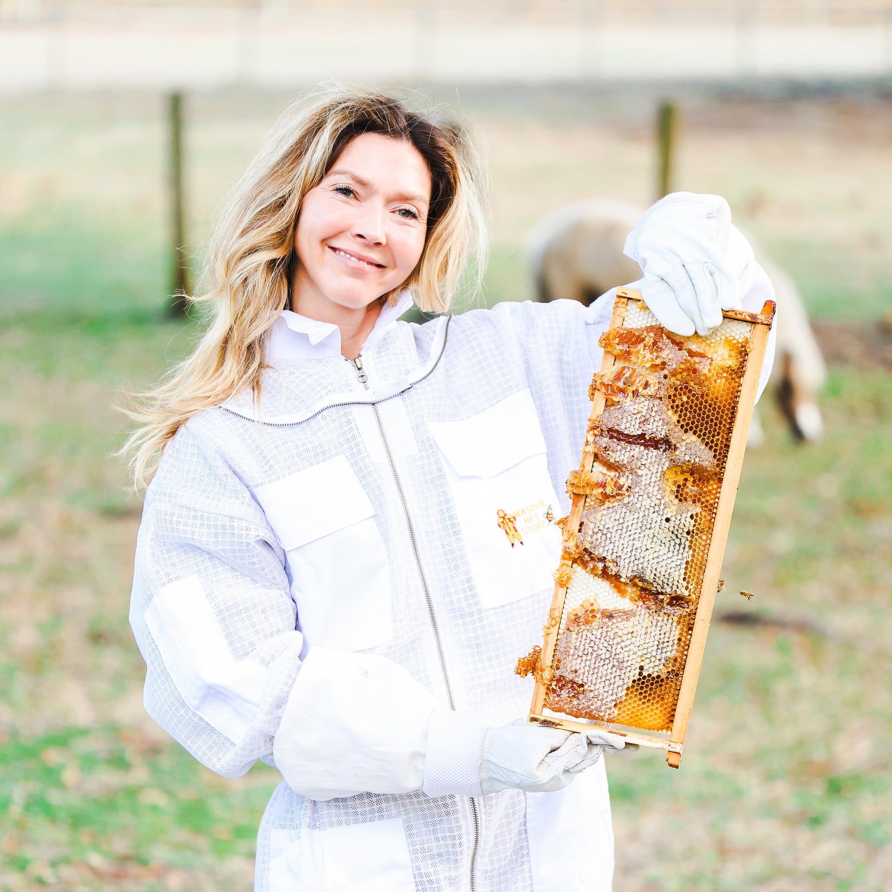 Woman in beekeeping suit holding a honeycomb frame outdoors