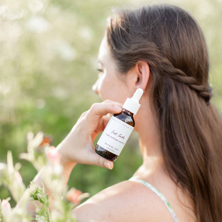 Lush Locks Batana Hair Oil bottle held near long hair outdoors with a soft natural background