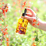 Hand holding a bottle of yellow liquid with a blurred natural background