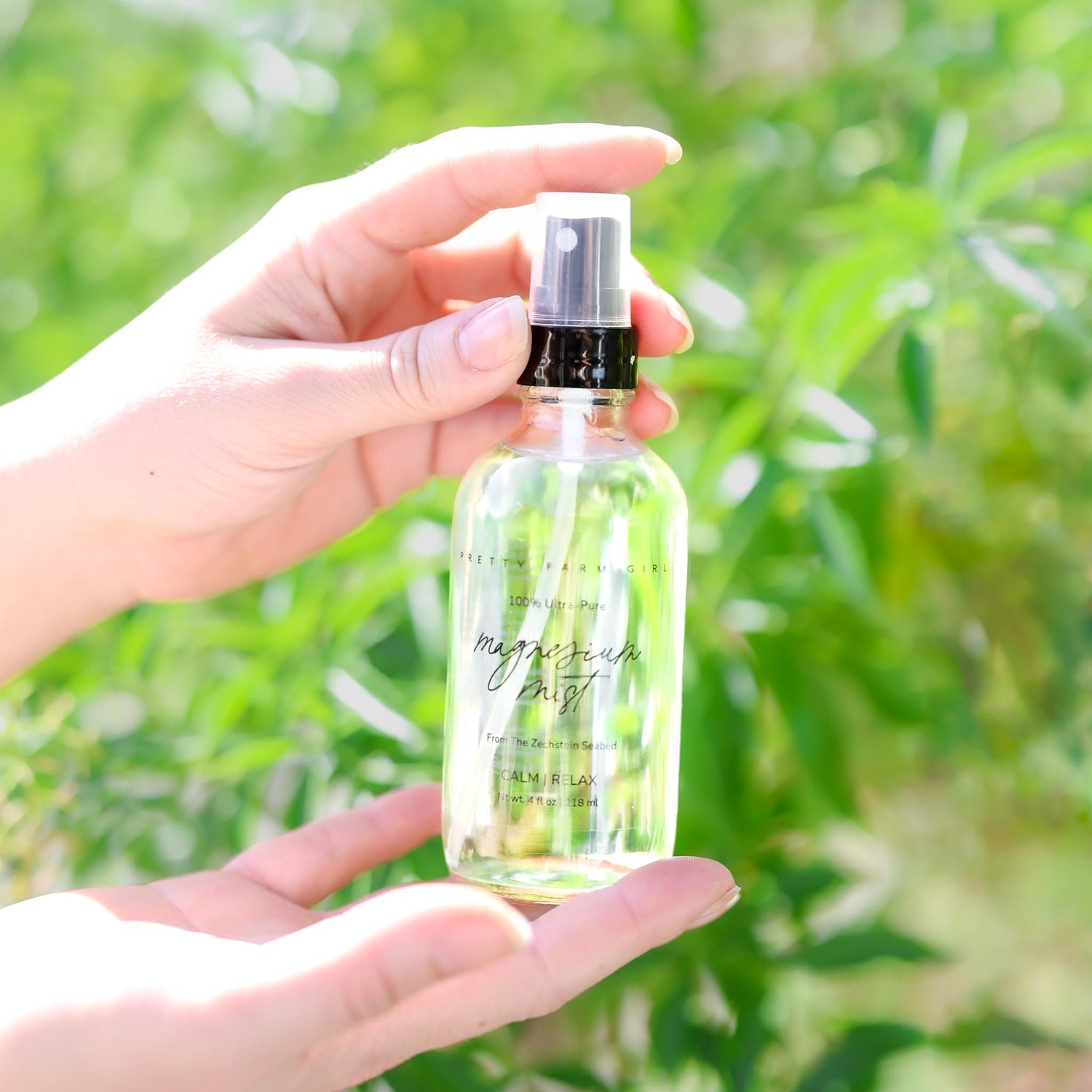 Hand holding a clear spray bottle with a green plant background