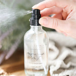 Hand holding a clear spray bottle labeled 'magnesium mist' with a blurred natural background