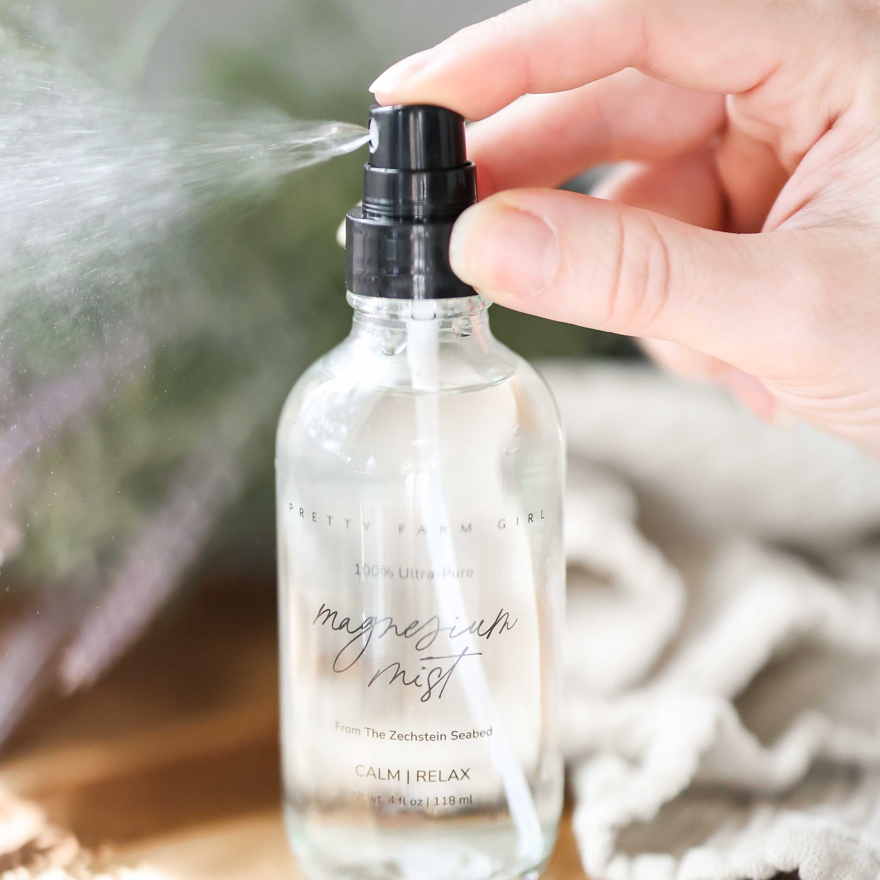 Hand holding a clear spray bottle labeled 'magnesium mist' with a blurred natural background