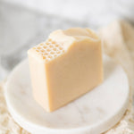 A rectangular bar of Milk & Honey Fragrance Free soap with a honeycomb pattern on one end, displayed on a small round white marble dish.