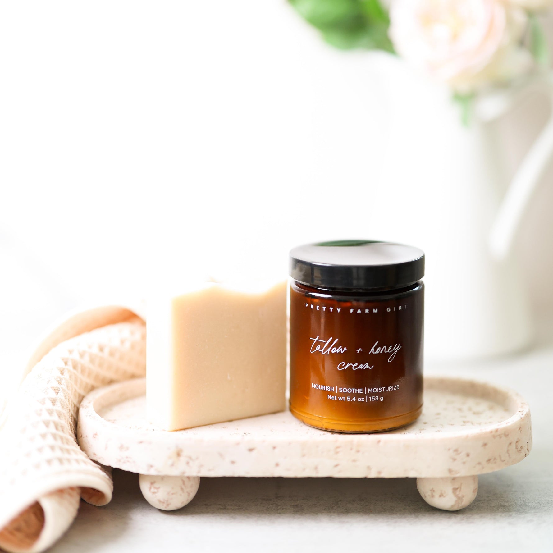 Pretty Farm Girl's fragrance free soap bar, and 5.4 glass amber jar of fragrance free Tallow + Honey Cream on a stone tray with soap and flowers in the background