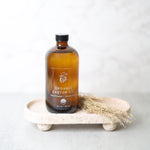 Amber glass bottle of Pretty Farm Girl's organic cold pressed hexane free castor oil on a white surface with a light gray background.