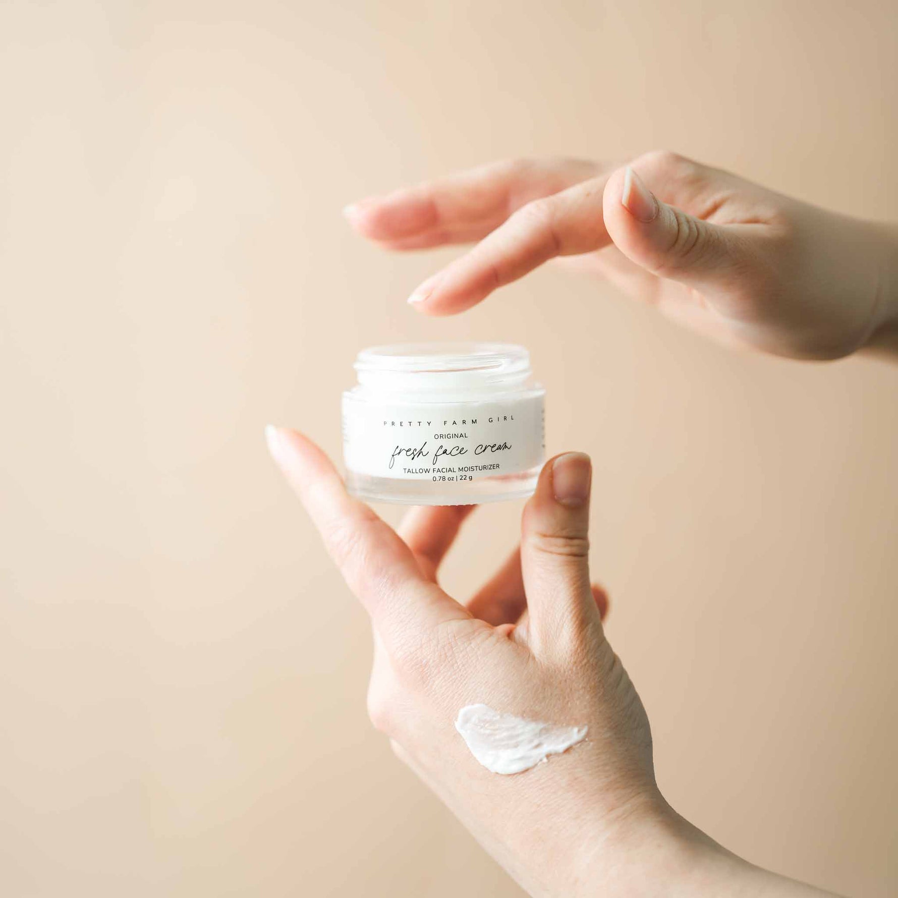 Person holding a jar of original face cream with a visible cream smear on the palm against a beige background
