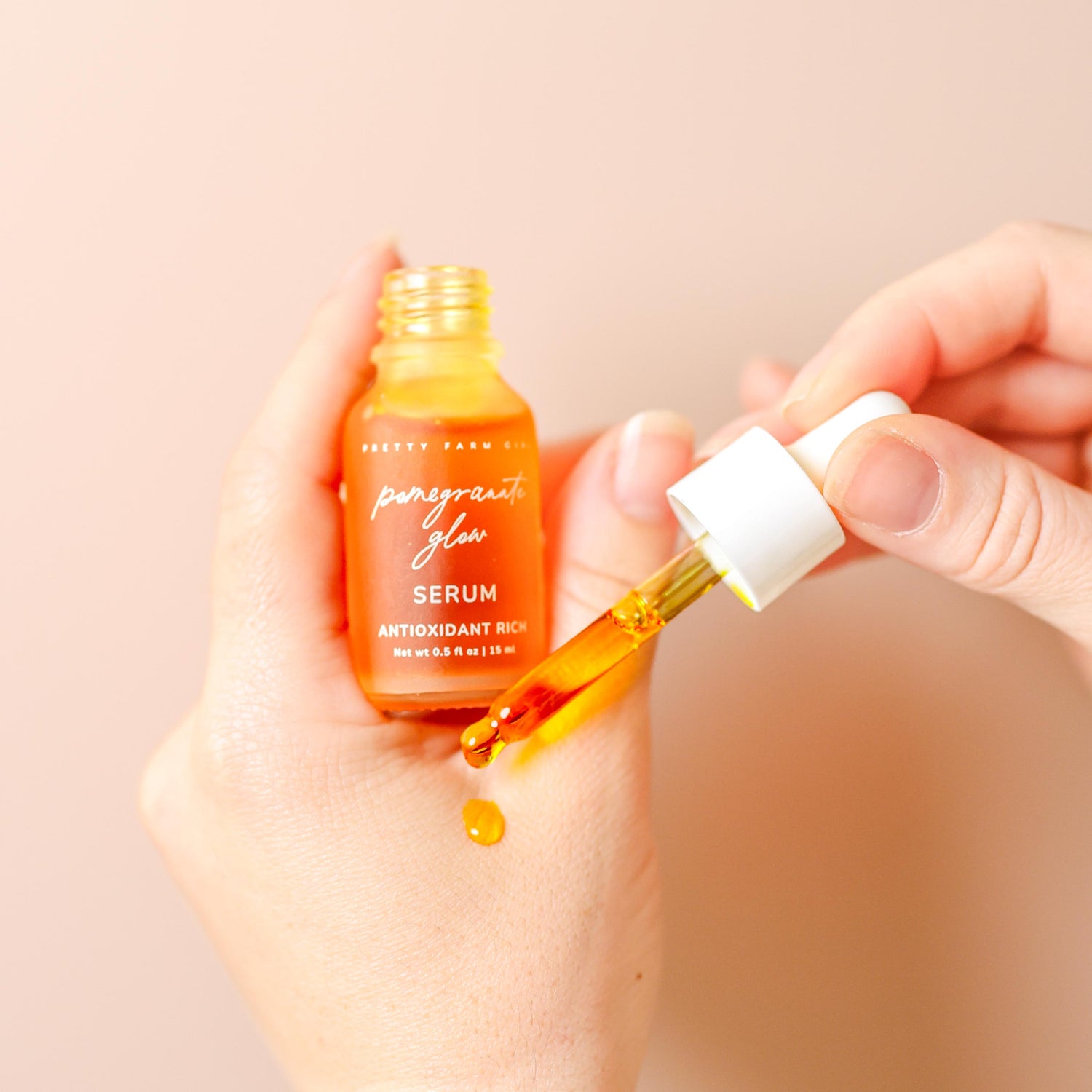 Hand holding a bottle of serum with dropper, against a beige background