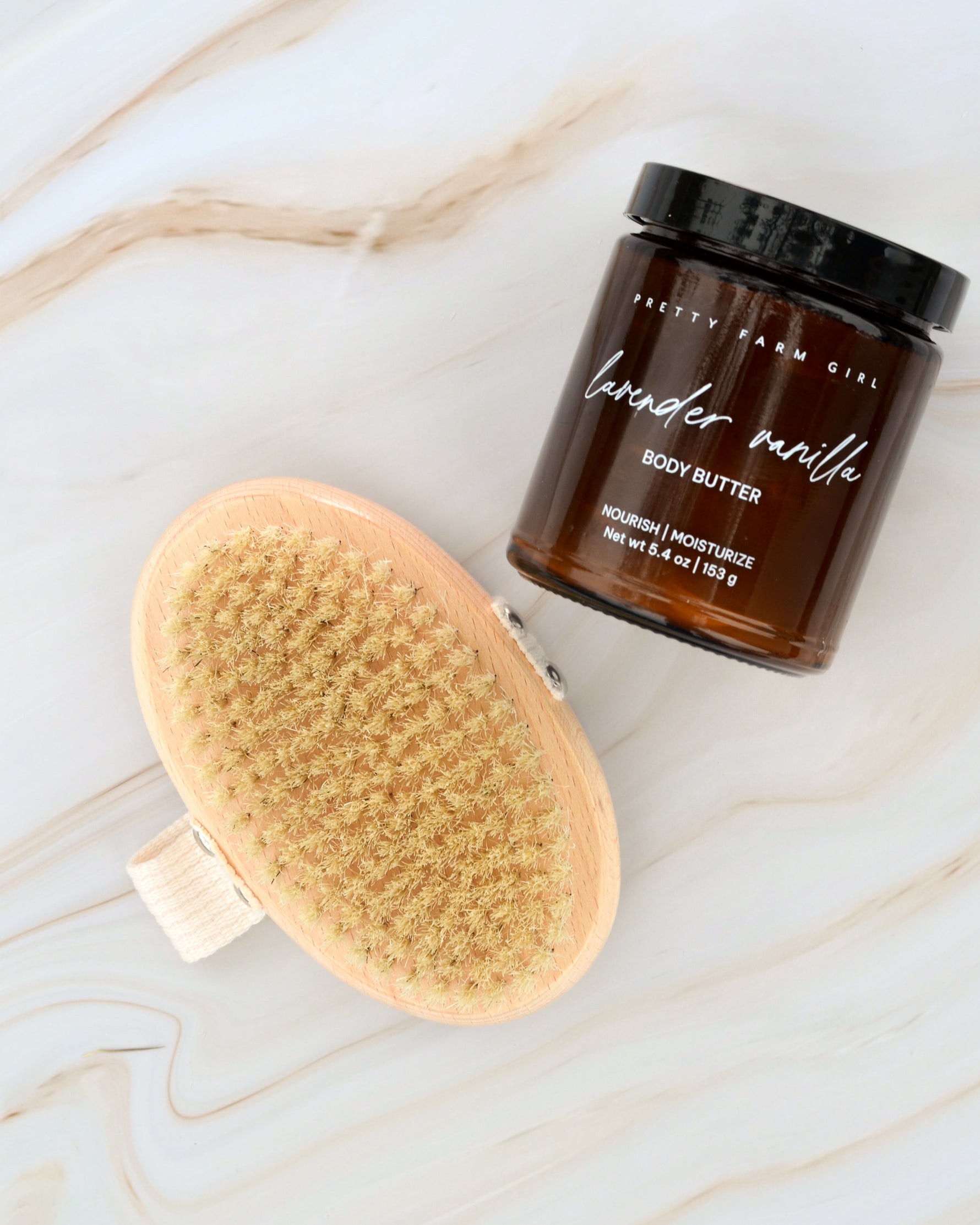 Pretty Farm Girl Lavender Vanilla Body Butter jar displayed next to a dry brush on a light marble background
