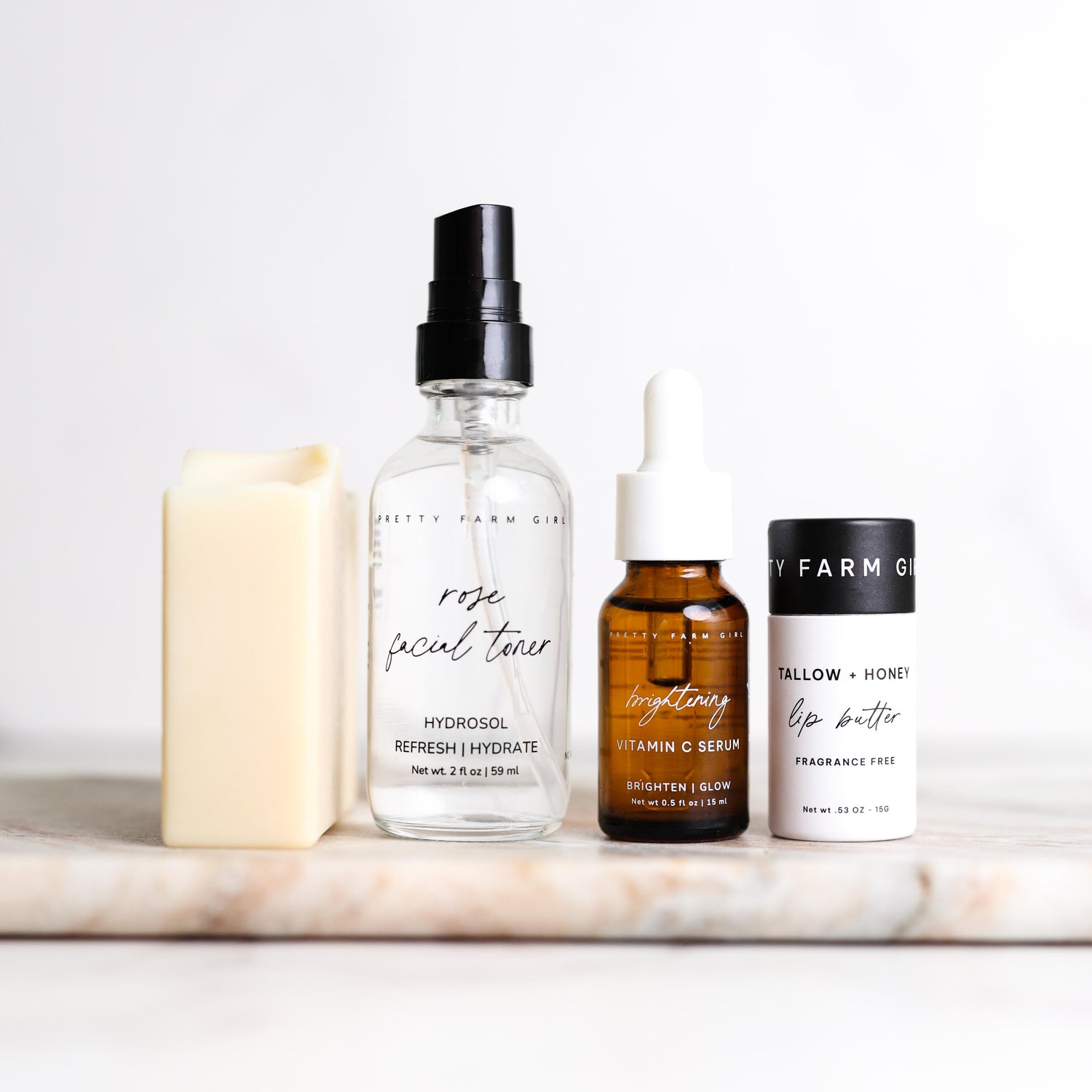 Pretty Farm Girl's Rooted and Ready Kit, showing 4 products including a Fresh Face Cream Soap Bar, 2oz Rose Facial Toner, .5oz Brightening Vitamin C Serum, .5oz Tallow + Honey Fragrance Free Lip Butter in an Eco-Friendly paper tube on a marble surface.