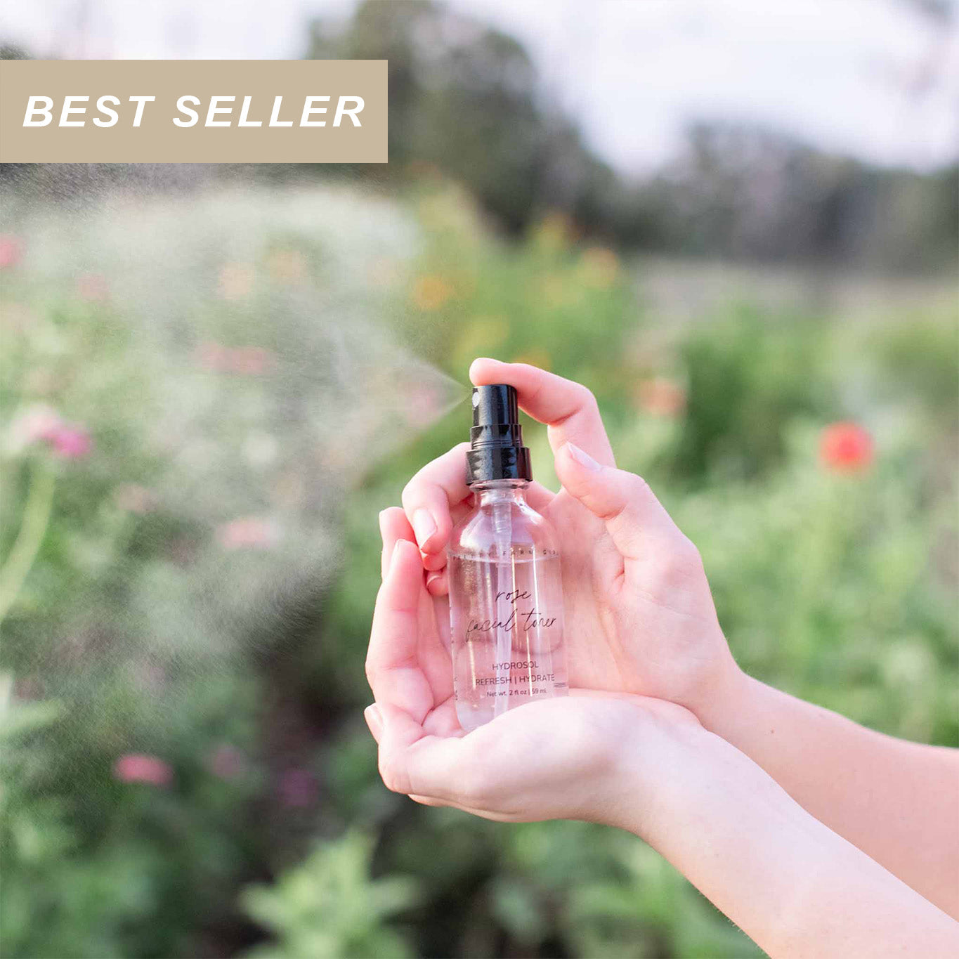 Hand holding a clear 2oz glass bottle of pure organic Rose Facial Toner hydrosol spraying outside with a natural floral background, and a best seller label in the corner
