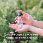 Hand holding a small toner hydrosol bottle with a natural floral background and text that says "Certified Organic | 100% Pure Natural Food-Grade Product"