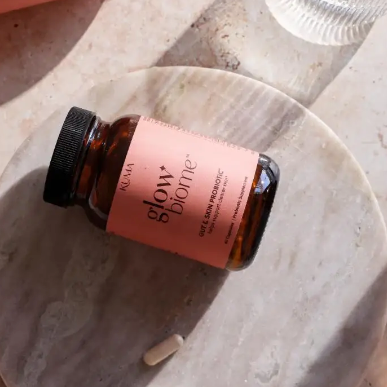 Glow Biome bottle on a marble surface with a glass cup of water in the background