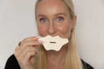Woman holding white mouth tape over her mouth against a plain background