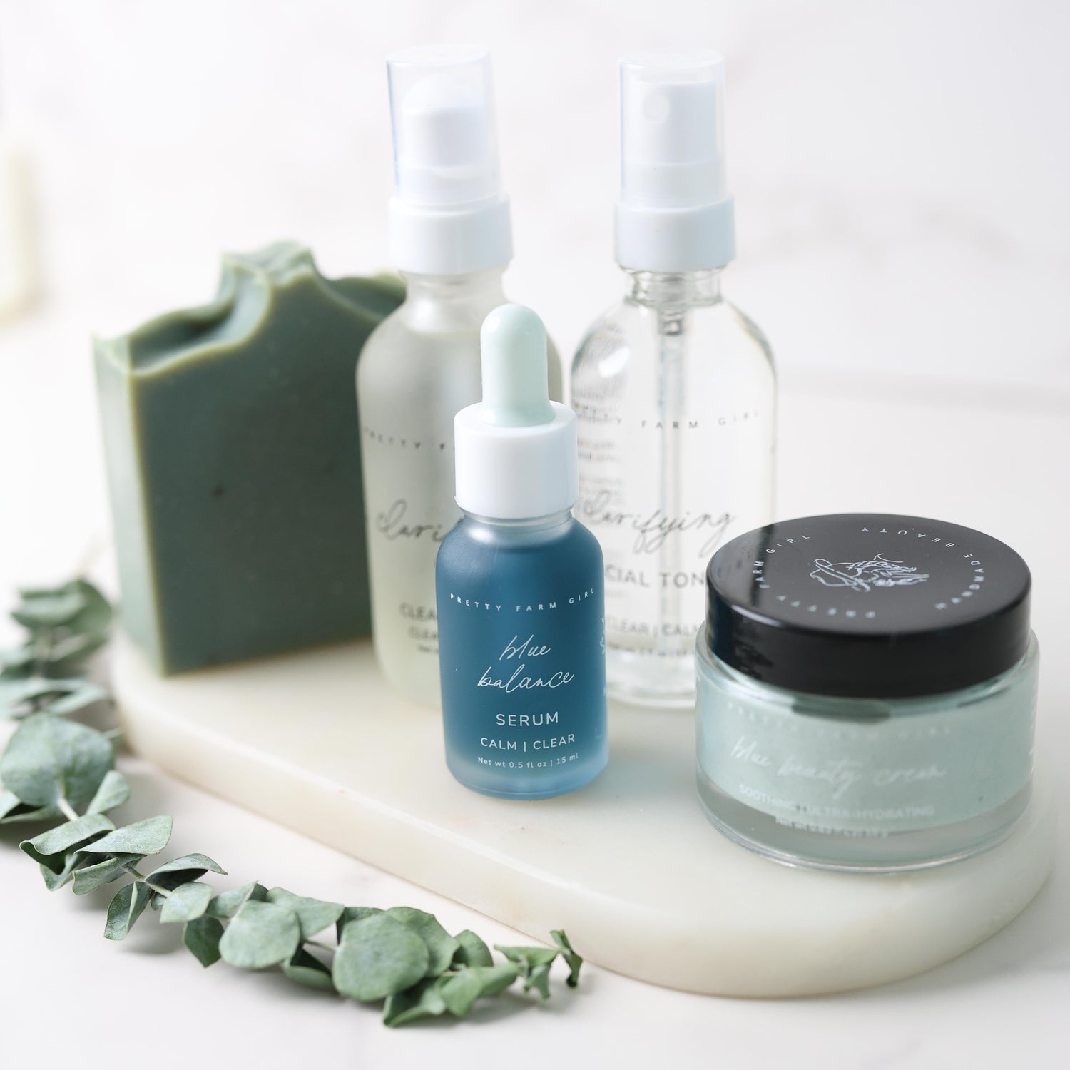 Skincare products including a serum, toner, and cream on a white surface with greenery.