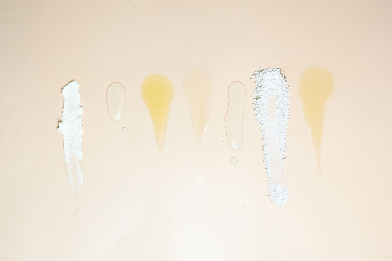 Skincare texture swatches, serum drops, and powder on a soft beige background.